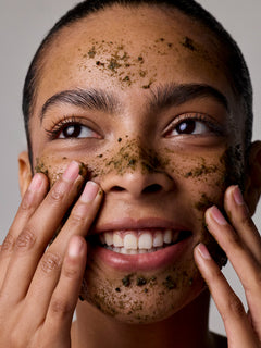 Person applying a facial scrub to their face with a neutral background