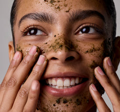 Person applying a facial scrub to their face with a neutral background