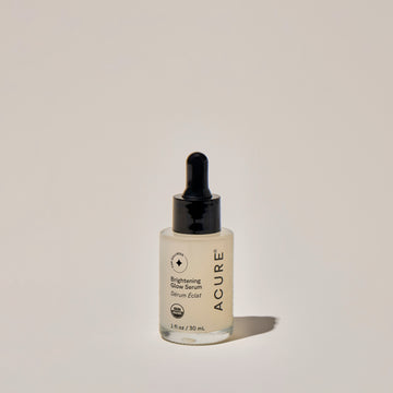 A clear glass bottle with a dropper containing the Brightening Glow Serum, labeled with the brand ACURE.