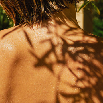 Shiny wet skin with leaf shadows on a blurred natural background