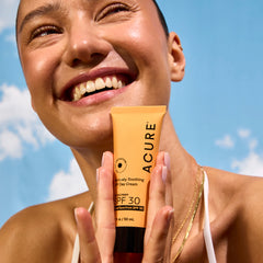 Woman holding a tube of Acure sunscreen against a blue sky.