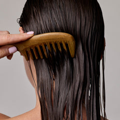 Person combing wet hair with a wooden comb against a neutral background