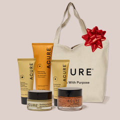Acure skincare products with a tote bag featuring a red bow on a light background