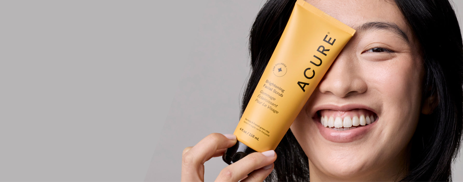 Person holding an Acure skincare product with a gray background