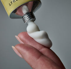 Close-up of a hand holding a tube of white cream against a gray background