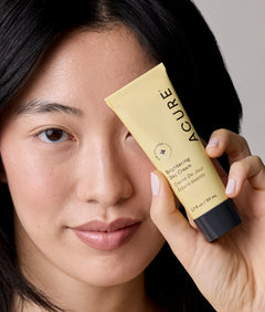 Person holding a Acure skincare product near their face