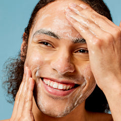Man applying a facial cleanser to his face against a blue background