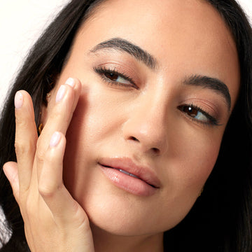 Close-up of a woman's face with one hand gently touching her cheek.