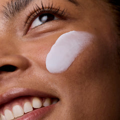 Close-up of a woman's face with a white cream applied to her cheek.