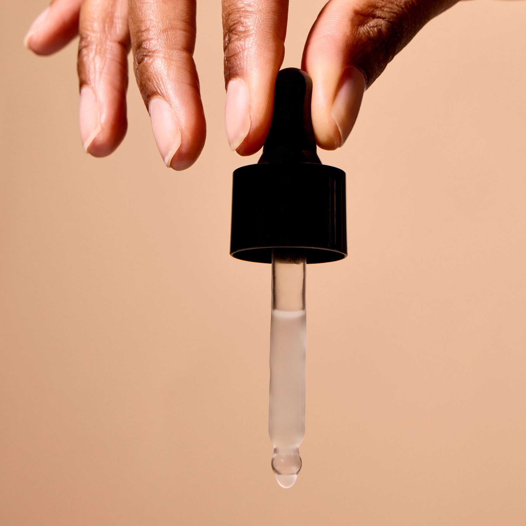 Hand holding a black dropper with clear liquid against a beige background