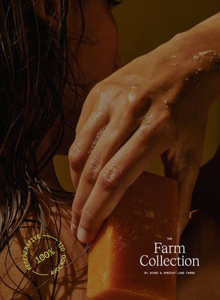 Hand holding a bar of soap next to green bottles with 'The Farm Collection' branding. image