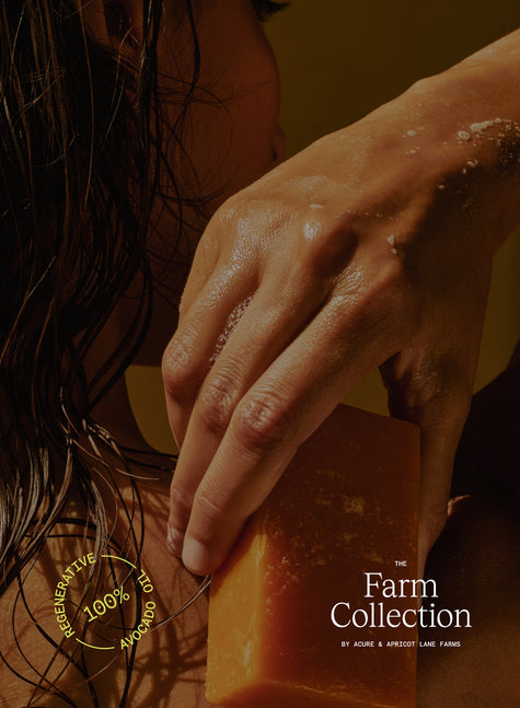 Hand holding a bar of soap next to green bottles with 'The Farm Collection' branding. image