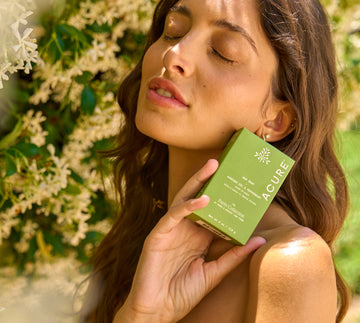 Woman holding a green Acure product box with flowers in the background