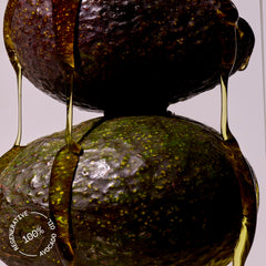 Close-up of an avocado with regenerative avocado oil dripping on it on a light gray background.