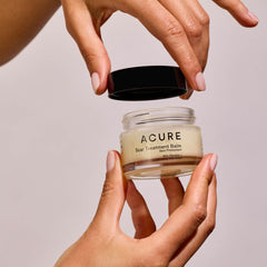 Acure scar treatment balm jar held by a hand against a neutral background