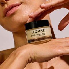 Acure Scar Treatment Balm jar held by a hand with a neutral background