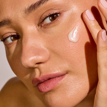 Close-up of a woman applying scar treatment balm to her face with a neutral background
