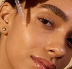 Close-up of a woman applying a dropper of skincare product to her face.