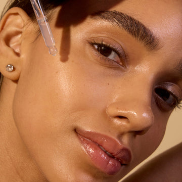 Close-up of a woman's face with a dropper applying liquid to her skin.