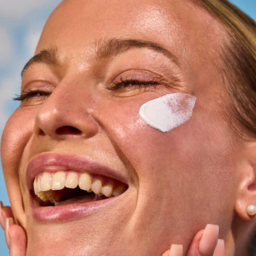 Woman applying sunscreen to her face with a blue sky background