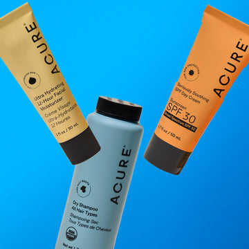 Acure skincare products including a facial moisturizer, dry shampoo, and sunscreen on a blue background