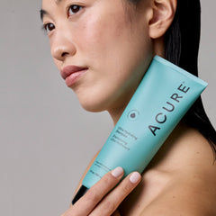 Person holding a tube of Acure Ultra Hydrating Shampoo against a neutral background